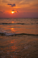 The image captures a stunning sunset over an ocean horizon with vibrant colors reflected in the water. Gentle waves add a serene feeling, perfect for depicting tranquility and the beauty of nature.