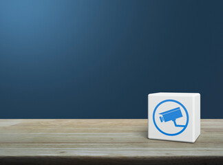 Cctv camera flat icon on white block cube on wooden table over light blue wall, Technology security and safety online concept