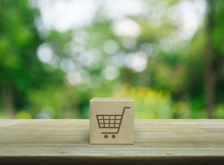 Shop cart flat icon on wood block cube on wooden table over blur green tree in park, Business shopping online concept