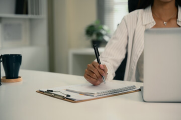 Businesswoman taking notes and working on laptop at modern workplace