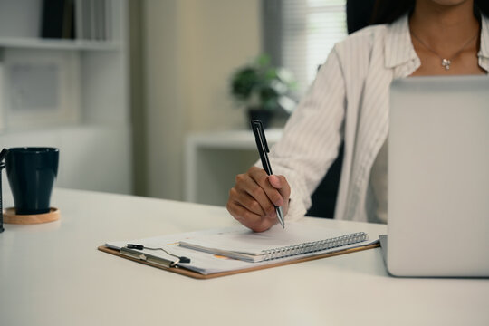 Businesswoman taking notes and working on laptop at modern workplace
