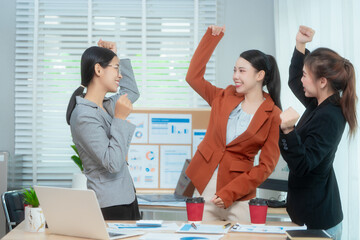 Three Asian women in formal suits collaborate at a desk, discussing documents in a modern office....