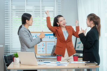 Three Asian women in formal suits collaborate at a desk, discussing documents in a modern office....