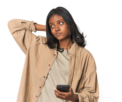 Young Indian woman using a smartphone touching back of head, thinking and making a choice.