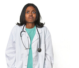 Young Indian doctor with stethoscope shrugs shoulders and open eyes confused.