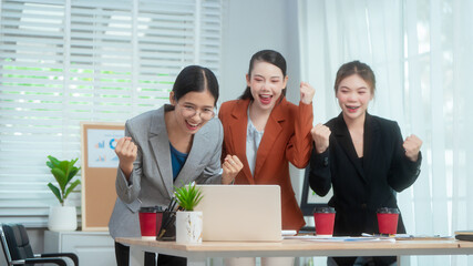 Three Asian women in formal suits collaborate at a desk, discussing documents in a modern office....
