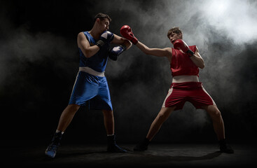Two boxers are engaged in an intense match surrounded by dramatic smoke in a dimly lit boxing ring....