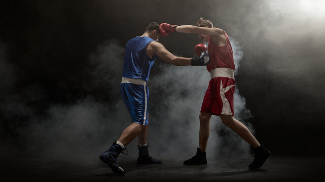Boxers in action deliver punches amid a smoky boxing ring atmosphere. Concept of intense sports competition and athletic determination.