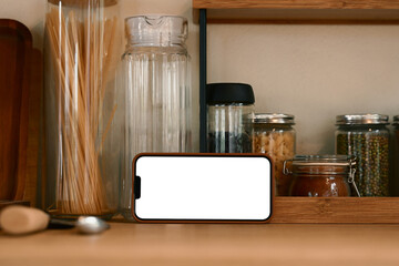 Smartphone with blank screen in horizontal position on a wooden kitchen counter
