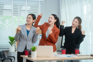 Three Asian women in formal suits collaborate at a desk, discussing documents in a modern office....
