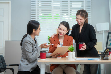 Three Asian women in formal suits collaborate at a desk, discussing documents in a modern office. teamwork, strategy planning, creative problem-solving in professional business environment.