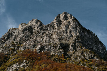 Majestic rocky mountain peak of Prokletije National Park in Montenegro rises above colorful autumn forest under clear blue sky.
