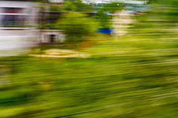 Dynamic motion blur view from high-speed train window: Green landscape, trees & fields rush past at high speed
