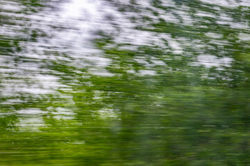 Dynamic motion blur view from high-speed train window: Green landscape, trees & fields rush past at...