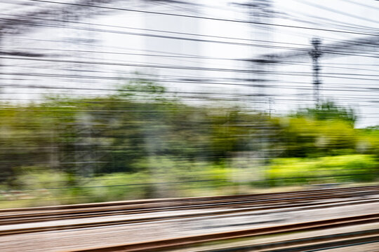 Dynamic motion blur view from high-speed train window: Green landscape, trees & fields rush past at high speed