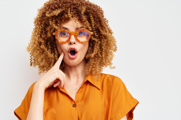 Surprised woman with curly hair wearing orange glasses and a shirt, expressing shock or disbelief...