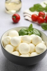 Tasty mozzarella cheese balls, tomatoes and basil on light grey table, closeup