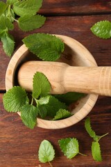 Fresh lemon balm leaves, pestle and mortar on wooden table, flat lay