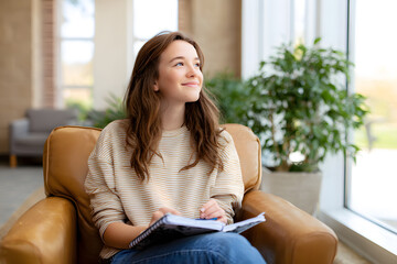 Obraz premium Teen girl smiling while journaling by the window, expressing emotions and thoughts in a cozy, sunlit interior. Mental health and self-reflection concept.