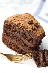 Piece of delicious chocolate cake with coffee beans and fork on plate, closeup