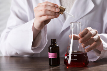 Professional perfumer developing luxury perfume at wooden table in laboratory, closeup