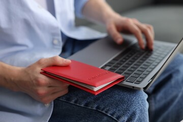 Man with passport using laptop indoors, closeup