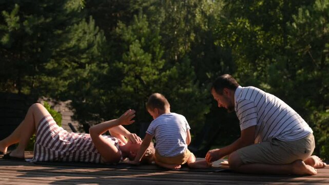 Mom, dad and son play jenga on the terrace in the summer sun street. Family vacation, child development. Game competition