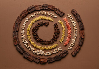 Various grains, spices and bark are arranged in a circle to resemble the "at" symbol (@) on a brown background.