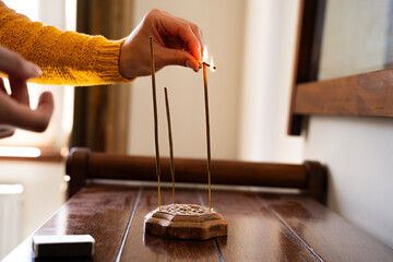 Woman lightning incense stick with match for aromatherapy, atmosphere and meditation in home setup...