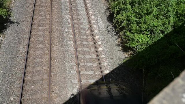 top view of a passenger train passing under a bridge, with parallel tracks framed by green vegetation. 4k footage