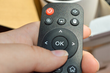 hand holding black remote control with projector box in background — perfect for tech product...