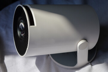modern white portable projector standing on a soft fabric surface in natural light. concept of home...