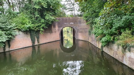 An ancient arch over still water forming a perfect circle. Surrounded by greenery, it feels like a...