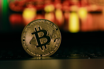 A shiny golden Bitcoin stands upright on a keyboard, symbolizing digital currency, blockchain...