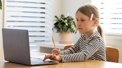Child studying online at home, sitting in front of laptop. Cute girl studying at online school. 