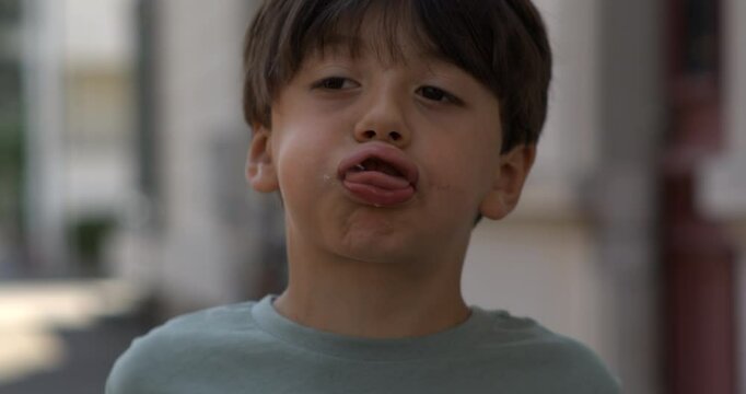 Young boy twisting tongue against lips in exaggerated silly face, captured in super slow motion with high-speed camera on city street during daytime