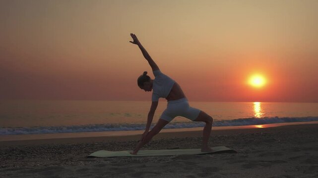 Woman Practicing Reverse Warrior Yoga Pose at Sunset on Beach