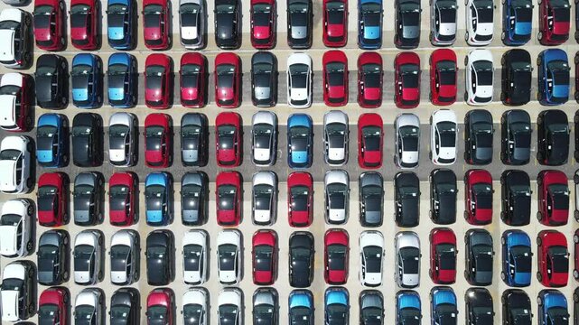 Aerial view of hundreds of cars neatly arranged by color in a distribution yard.