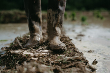 Close-up of feet covered in mud, standing on wet, muddy soil in an outdoor, natural environment.