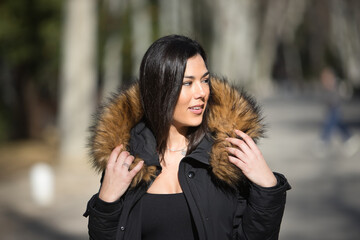Portrait of a young, beautiful, dark-haired woman, looking distracted, wrapping herself up with the fur collar of her coat, on a cold and sunny day. Concept winter, cold, autumn, weather.