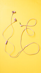 Flat lay of pink wired earphones with a 3.5mm jack and inline mic, displayed on a vibrant yellow...