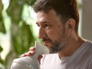 A middle aged man uses a steam inhaler for respiratory health while sitting indoors, surrounded by...