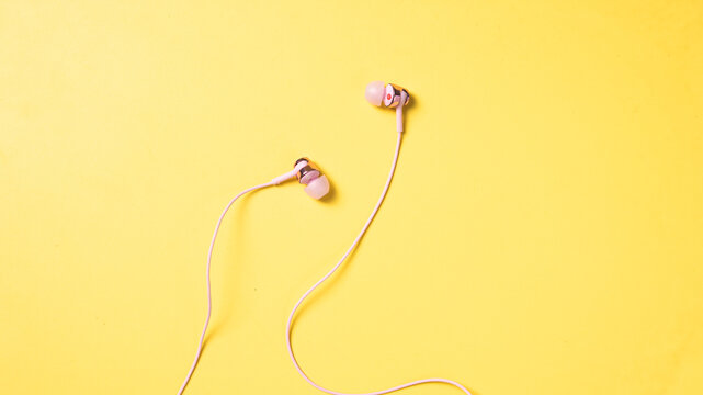 Flat lay of pink wired earphones with a 3.5mm jack and inline mic, displayed on a vibrant yellow background, perfect for lifestyle, music, or tech-related content