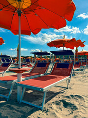 Beach chairs with orange umbrellas on a sandy beach. Empty chairs on a sunny day. Vertical photo