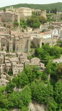 Aerial summer afternoon view of Sorano. Rooftops of an ancient medieval hill town hanging from a tuff stone over the Lente River. Etruscan heritage. Province Grosseto, Tuscany, Italy. Vertical footage