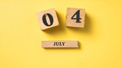 Wooden blocks arranged to show the date July 4 on a bright yellow background. A simple and symbolic...