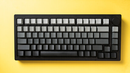 Minimalist mechanical keyboard with gradient gray keycaps placed on a vibrant yellow background,...