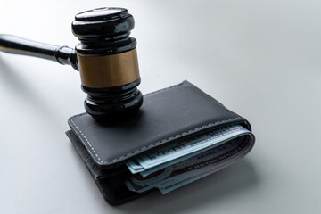A judge's gavel on a wallet overflowing with US hundred-dollar bills. Wage garnishment, fines, legal fees concept.