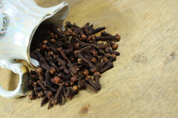 Dried cloves spilling from a vintage ceramic cup onto a wooden surface. Aromatic spice concept for culinary, herbal medicine, and organic product visuals