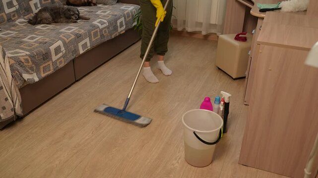 A homemaker is mopping the floor with a mop, making sure not to miss a single stain. This involves using a mop for cleaning the floors and maintaining order and cleanliness in the house.